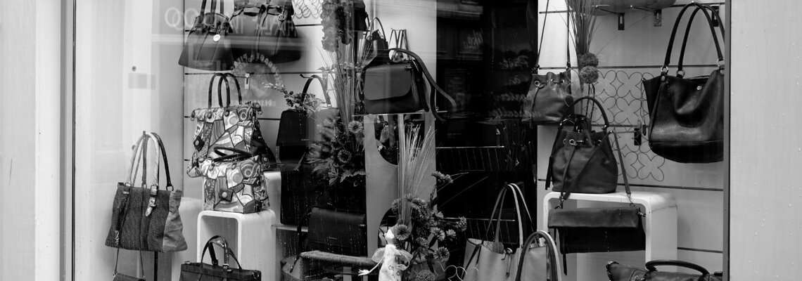 Es ist ein Schaufenster mit vielen unterschiedlichen Taschenmodellen zu sehen. Das Bild ist in schwarz-weiß Optik.