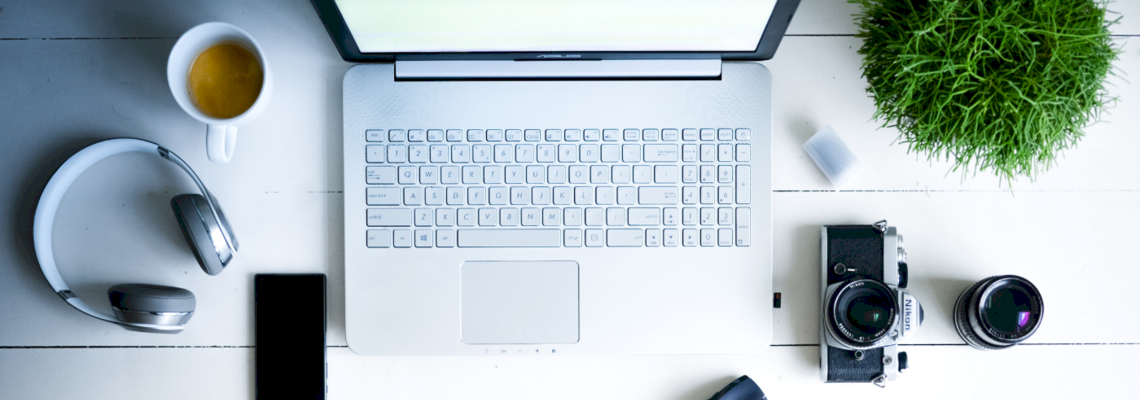 Ein Laptop, Handy und verschiedenes Reisezubehör liegen auf einem Tisch.