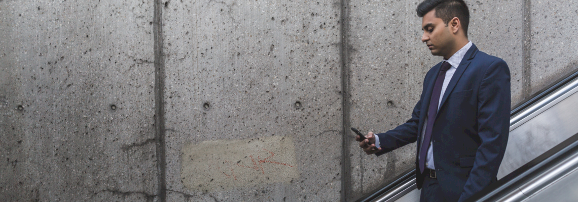 Auf dem Banner ist ein Mann in einem dunkel blauen Anzug abgebildet, der auf einer Rolltreppe steht und auf sein Handy schaut.